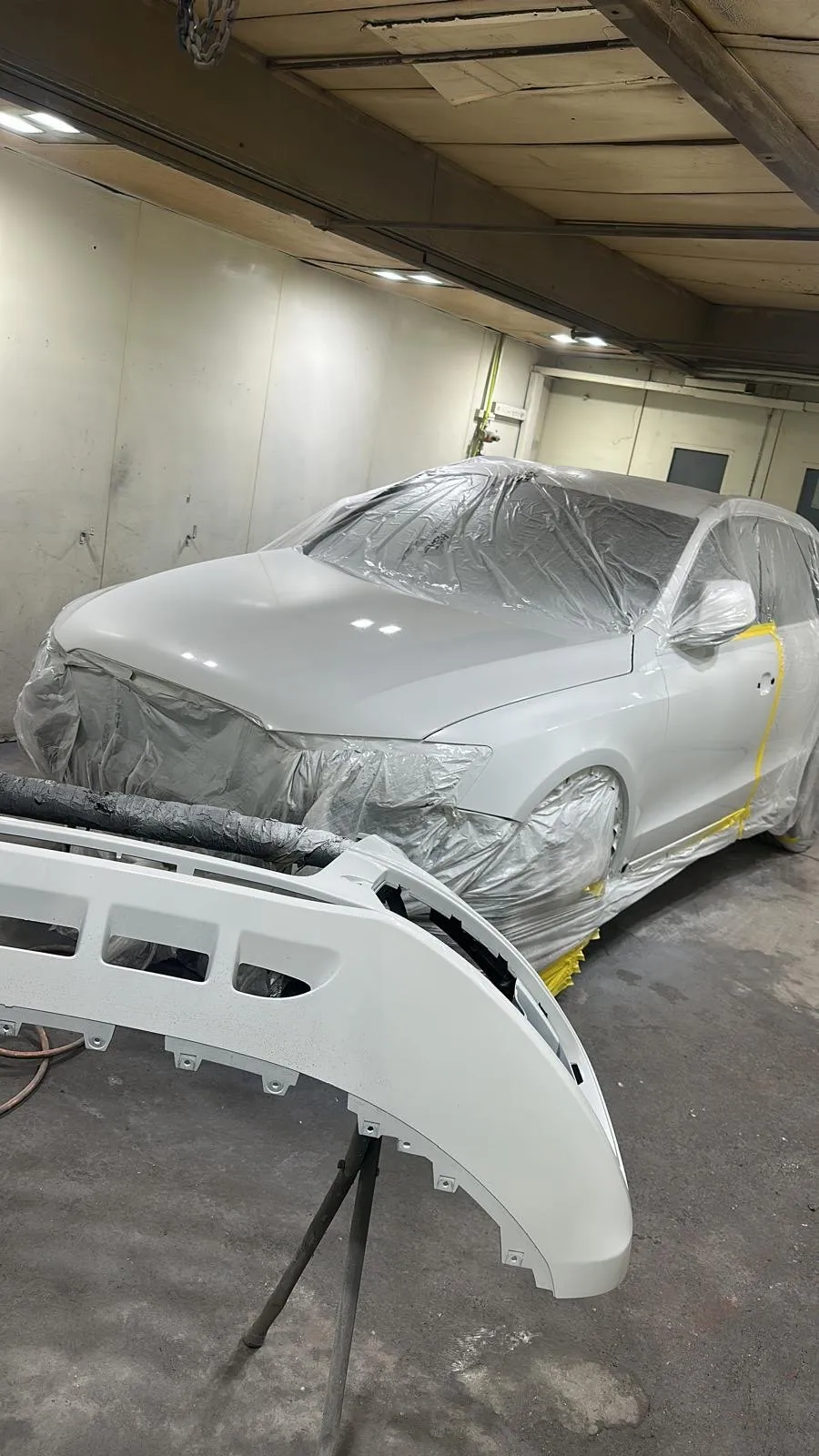Bumper in primer, the car masked behind it in the booth